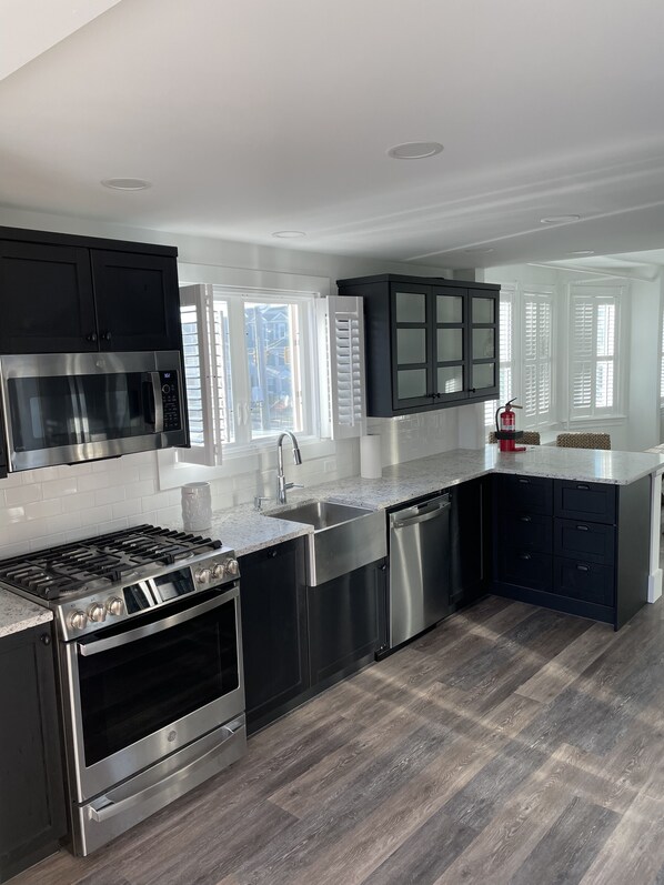 A modern kitchen with stainless steel appliances, black cabinets, and a herringbone wood floor.