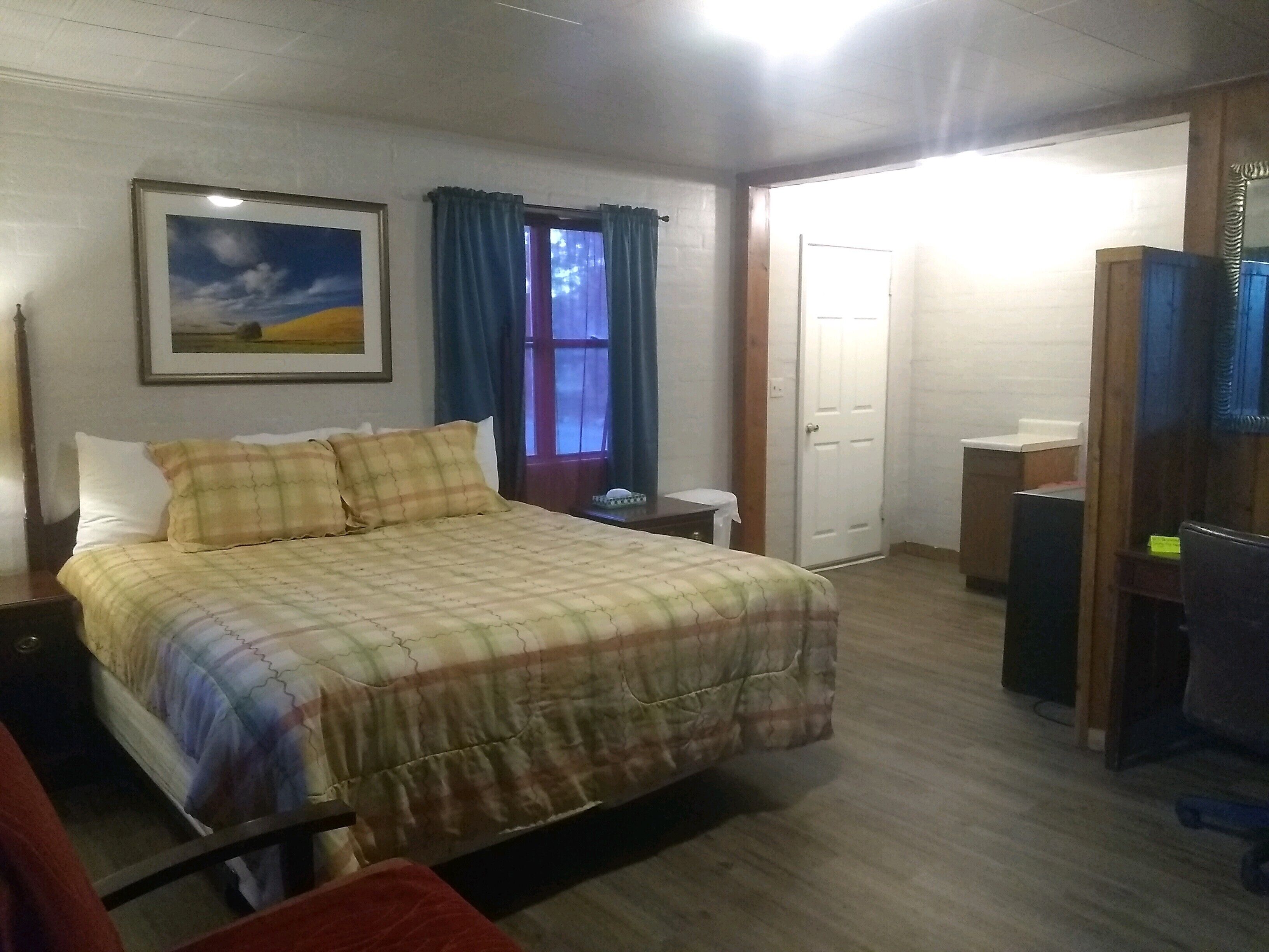 Un dormitorio con cama, mesita de noche, cómoda, espejo, puerta y ventana con cortinas.