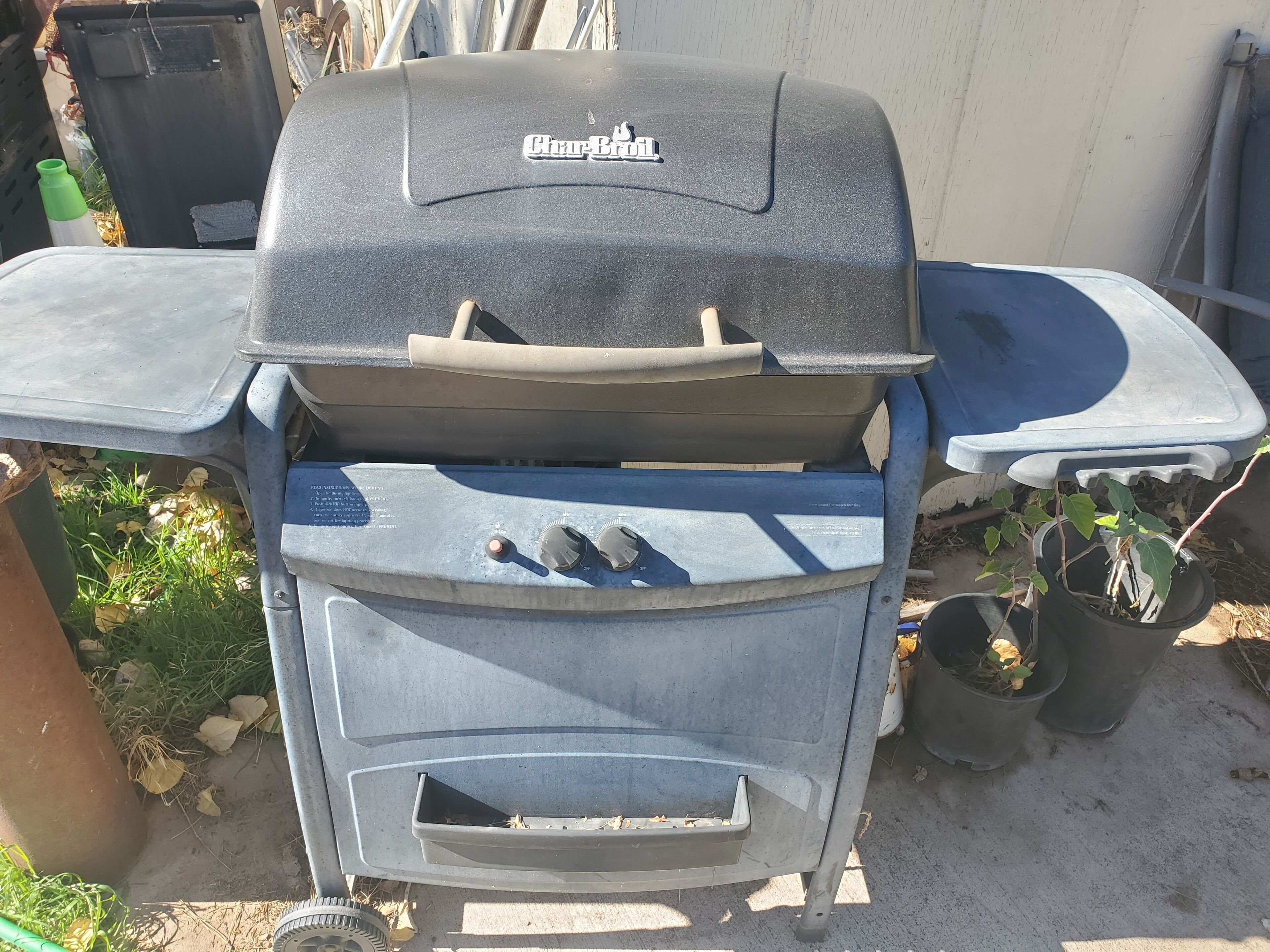 Ein Char-Broil Grill mit Bedienfeld, einer seitlichen Ablage und einem Blumentopf in der Nähe.