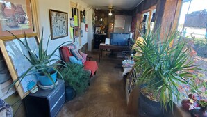 A cozy interior with a wooden ceiling, a large window, and various plants and artwork.