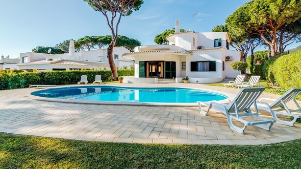 Una villa moderna con piscina, sillas de descanso y un jardín bien cuidado.
