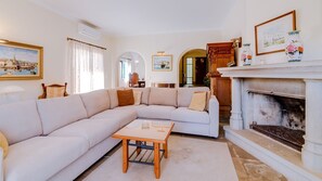 A living room with a beige sectional sofa, a wooden coffee table, a fireplace, and a painting on the wall.