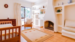 Una sala de estar acogedora con chimenea, una silla de madera, un sofá y una estantería llena de libros y objetos decorativos.