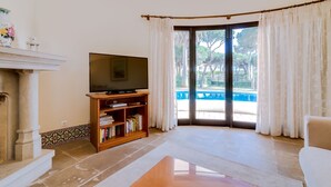 Una sala de estar con televisor, estanterías, chimenea y vista a una piscina.
