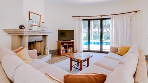 Una sala de estar con chimenea, televisor, un conjunto de sofás y vista a una piscina.