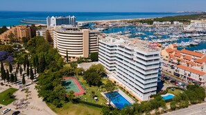 A high-rise hotel with a rooftop pool, surrounded by lush greenery and a marina with boats.