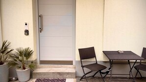 Une porte dotée d’une poignée, une caméra de surveillance et une petite marche menant à un patio équipé de deux chaises et d’une table.