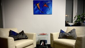 Un salon moderne avec deux canapés en cuir beige, chacun agrémenté d’un coussin foncé. Une table basse en verre, sur laquelle repose un objet rouge, se trouve entre les canapés. Un tableau abstrait bleu est accroché au mur, au-dessus de la table basse.