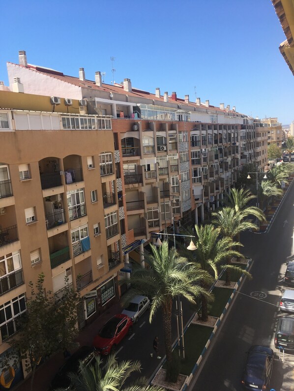 A multi-story residential building with balconies, a street view, and palm trees.