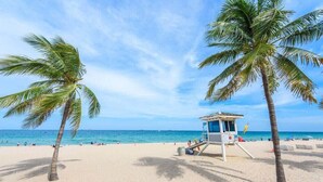 A beach with palm trees, a lifeguard tower, and the ocean in the background. - Posturepedic Beds!NearBeach/Airport Spacious BBQ/BAR (Miami)