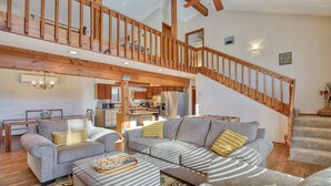 Ein geräumiger Wohnbereich mit einer hohen Holztreppe, einer Küche im Hintergrund und einer gemütlichen Sitzecke.