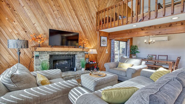 Ein gemütliches Wohnzimmer mit Kamin aus Stein, einem an der Wand montierten Fernseher und einem Essbereich mit Holztisch und Stühlen.