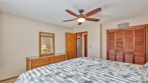 A bedroom with a bed, a dresser, a mirror, a ceiling fan, and a closet.
