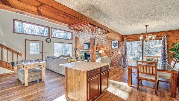 A cozy cabin interior with a wooden-floored living area, a central island, a dining table, and a fireplace.