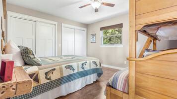 A bedroom with a bed, a wooden dresser, a ceiling fan, and a window with a view of trees.