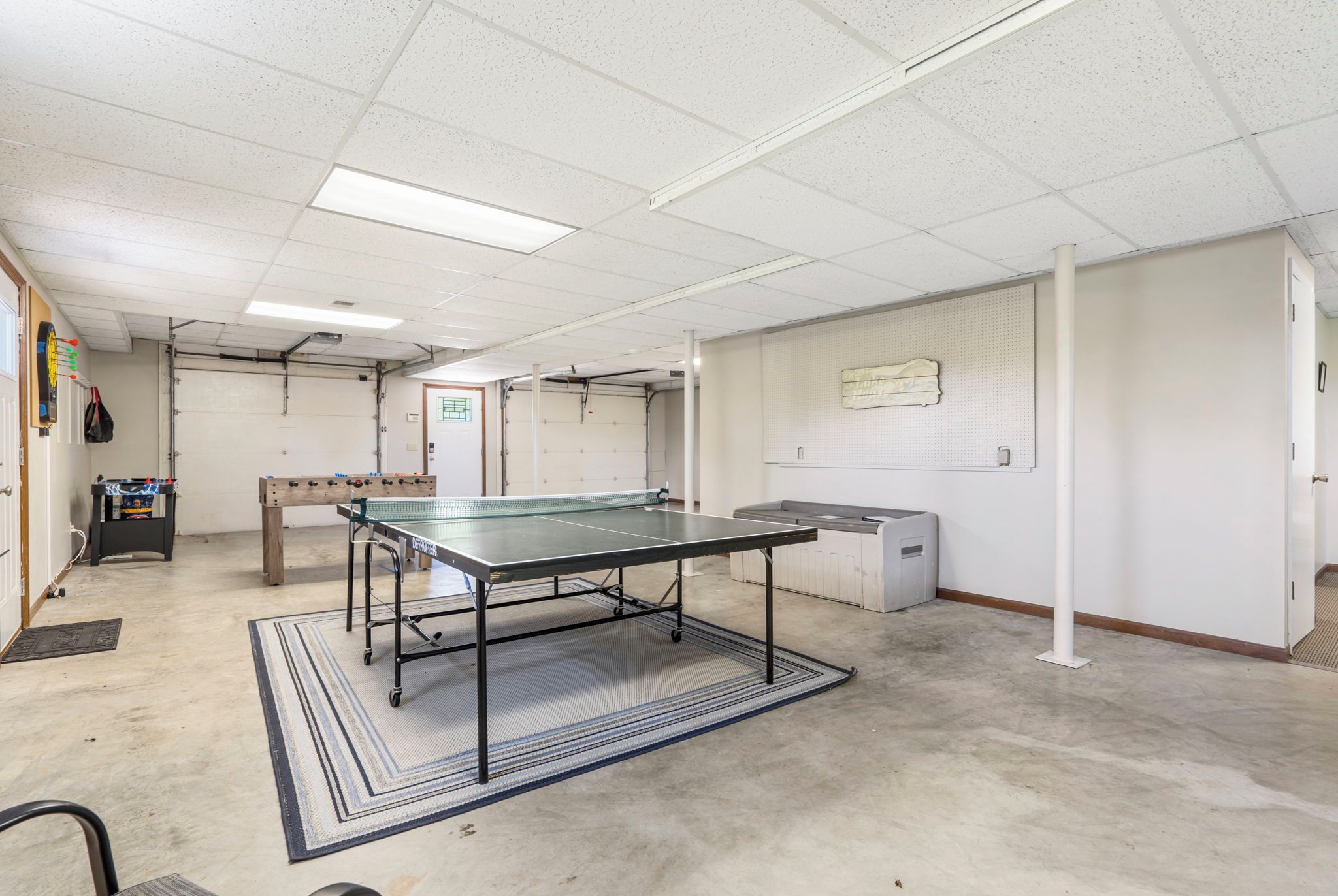 A room with a ping pong table, a foosball table, and a small cabinet.
