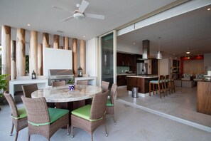 A spacious outdoor dining area with wicker chairs and a marble table, connected to a kitchen and living space.