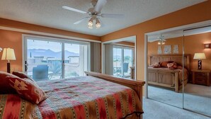 Ein Schlafzimmer mit einem großen Bett, einem Deckenventilator, einem Fenster mit Bergblick und einem Spiegel, der den Raum widerspiegelt.
