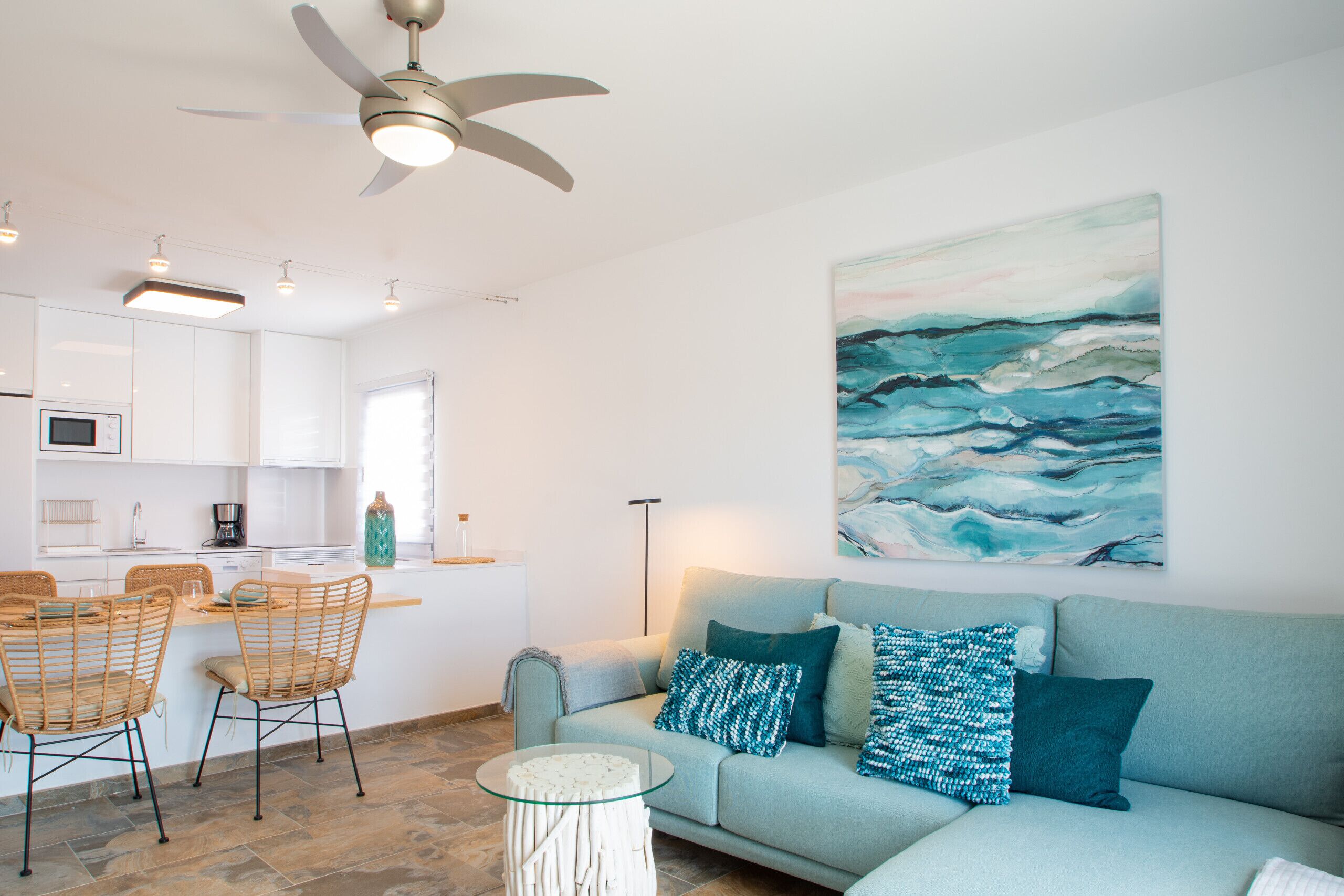 A modern living space with a kitchen, dining area, and a large artwork of ocean waves.