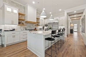 Una cocina moderna con armarios blancos, una isla central con taburetes y luminarias colgantes.