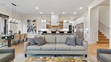 Un salon moderne avec un canapé gris, des coussins à motifs, une table basse en marbre et un coin repas comprenant une table et des chaises blanches.
