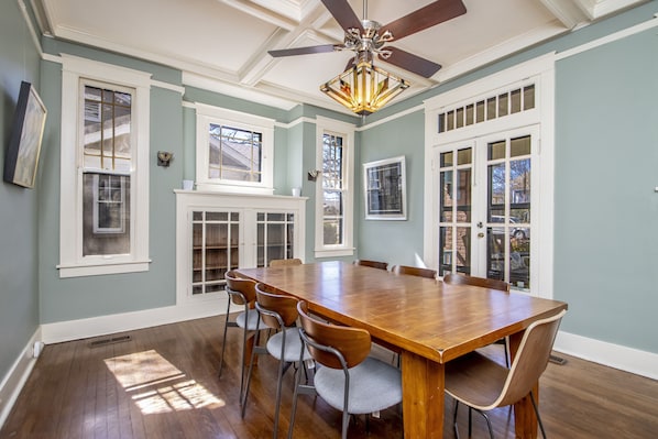 A dining room with a large wooden table and six chairs, a ceiling fan, and a fireplace.