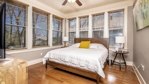 Un dormitorio con una cama grande, suelo de madera y varias ventanas con persianas.
