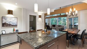 Una cocina moderna con encimera de granito, un comedor con mesa y sillas de madera, y un ventanal que ofrece vistas al exterior.