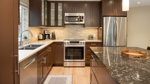 Una cocina moderna con gabinetes marrón oscuro, electrodomésticos de acero inoxidable, una encimera de granito y una tabla de cortar de madera.
