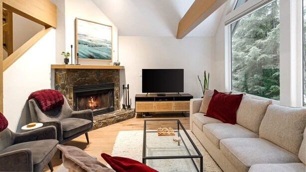 Una sala de estar moderna con chimenea de piedra, televisor de pantalla plana y un ventanal con vistas a árboles.