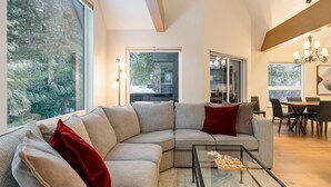 Una sala de estar moderna con un amplio sofá seccional, una mesa de centro de vidrio y un comedor con una mesa y sillas de madera.