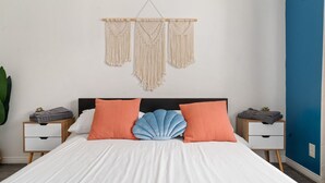 Un dormitorio con cama, dos mesitas de noche, un colgador de macramé y una pared azul decorativa.