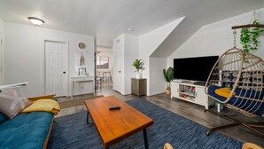 Una sala moderna con un sofá, una mesa de centro de madera, un sillón colgante y un televisor.