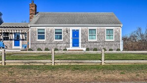 A two-story house with a blue door and windows, a brick chimney, and a wooden fence in front.