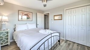 A bedroom with a bed, a ceiling fan, a nightstand with a lamp, and a door.