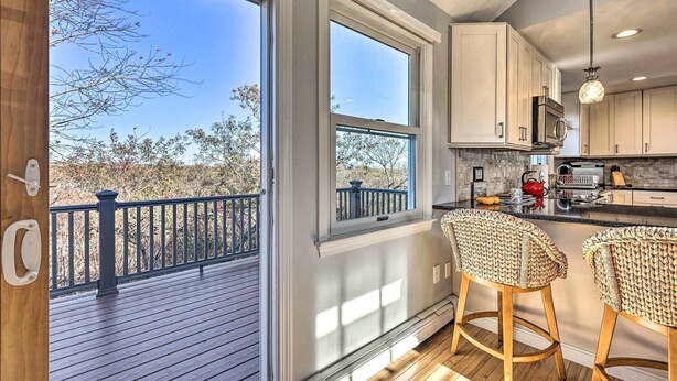 A modern kitchen with a large window, wooden deck, and two wicker bar stools.