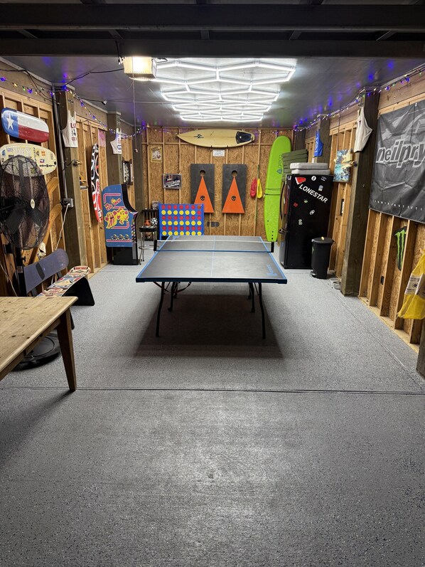 A ping pong table in a room with wooden walls, a ceiling fan, and various sports equipment.