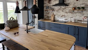 Una cocina moderna con encimera de madera, armarios oscuros y una pared de ladrillo como protector.