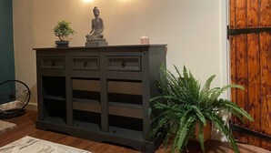 Una consola de madera oscura con una estatua de Buda, dos bombillas colgantes y una planta en maceta.