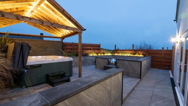 Un patio con jacuzzi, parrilla y un pérgola con luces.