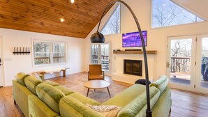 Un salon spacieux avec un canapé vert, un plafond en bois, une cheminée et de grandes fenêtres.