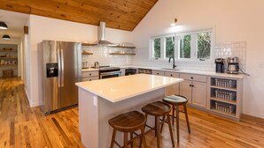 Une cuisine moderne dotée d’un îlot central, de planchers en bois et offrant une vue sur la verdure environnante.