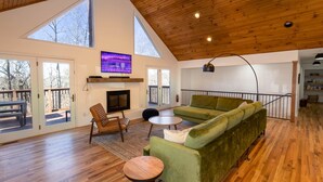 Un salon spacieux avec un canapé vert, un plancher en bois, une cheminée et un téléviseur fixé au mur.