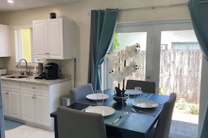 A dining area with a table set for two, a coffee maker, and a potted orchid.