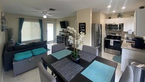 A modern living room with a sofa, dining table, and kitchen area with appliances.