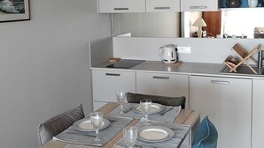 A modern kitchen with white cabinets, a dining table set for four, and a pendant light above. - Appartement Face MER - La Baule (LA BAULE ESCOUBLAC)