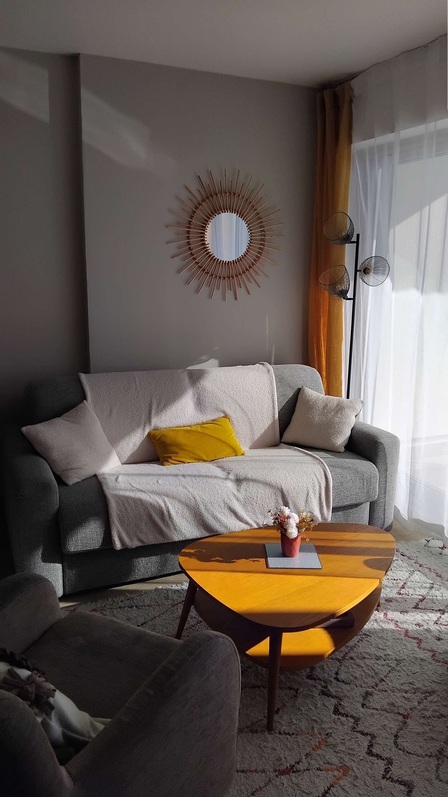 Een woonkamer met een bank, een salontafel, een spiegel en een lamp.