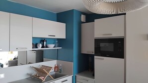 A modern kitchen with white cabinets, a black microwave, and a blue accent wall. - Appartement Face MER - La Baule (LA BAULE ESCOUBLAC)