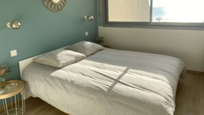 A bedroom with a bed, a window, a wall-mounted mirror, and a small table with a vase. - Appartement Face MER - La Baule (LA BAULE ESCOUBLAC)