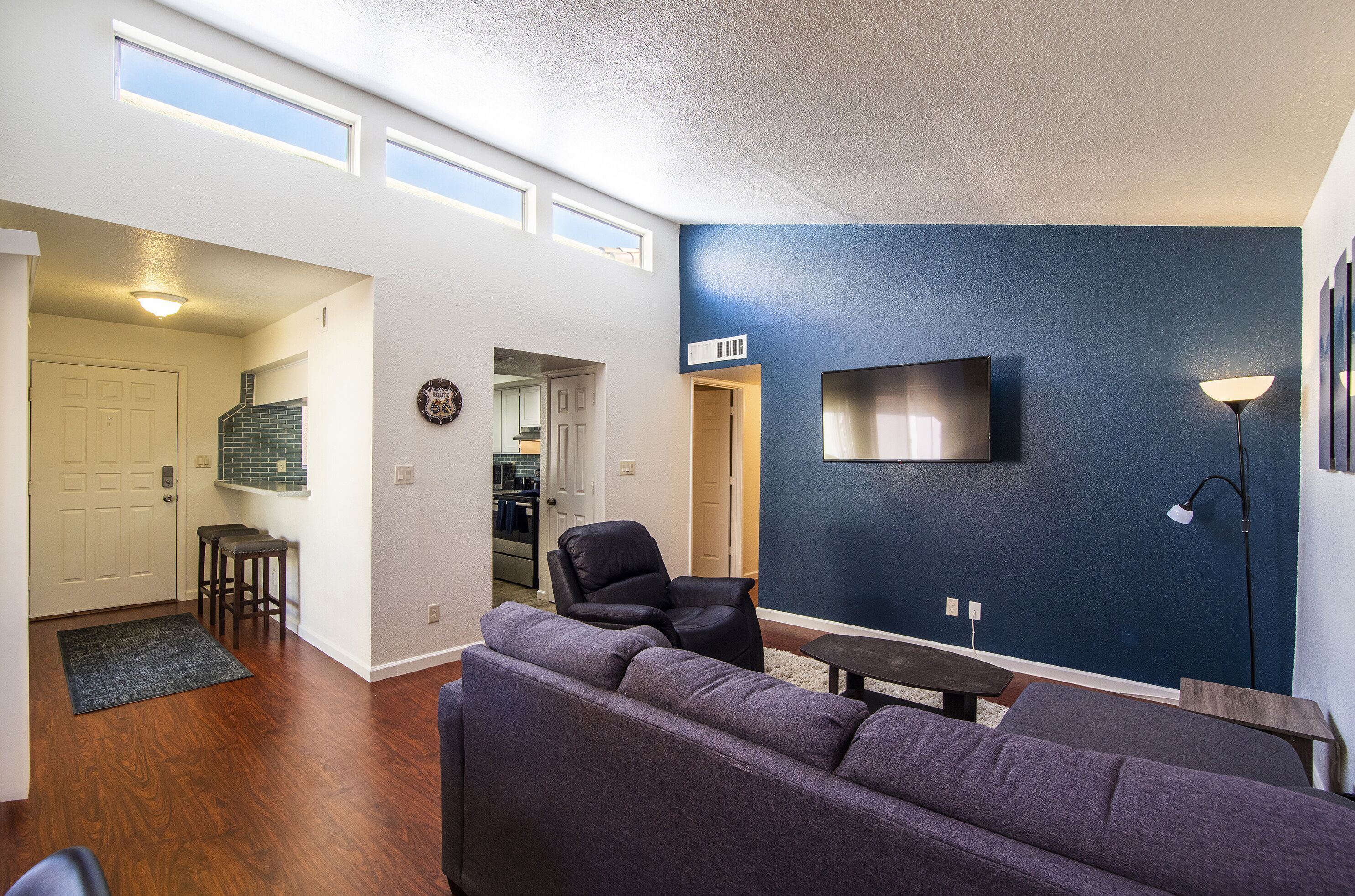 A living room with a dark blue accent wall, a flat-screen TV mounted above a wooden coffee table, and a large gray sectional sofa.
